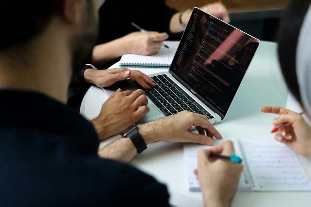 Tim kecil berdiskusi mengelilingi satu laptop di meja rapat