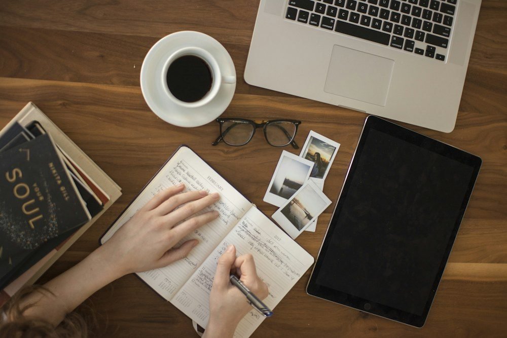Penulis blog mengetik di laptop sambil mencatat di buku harian